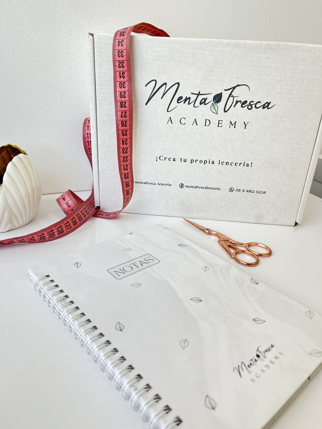 Caja del taller Menta Fresca Academy con huincha de medir, tijera cobre y cuaderno de notas.