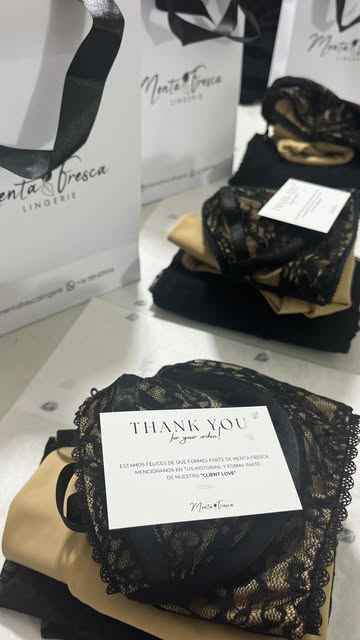 Prendas de encaje negro y satén champán empacadas en bolsas de Menta Fresca.