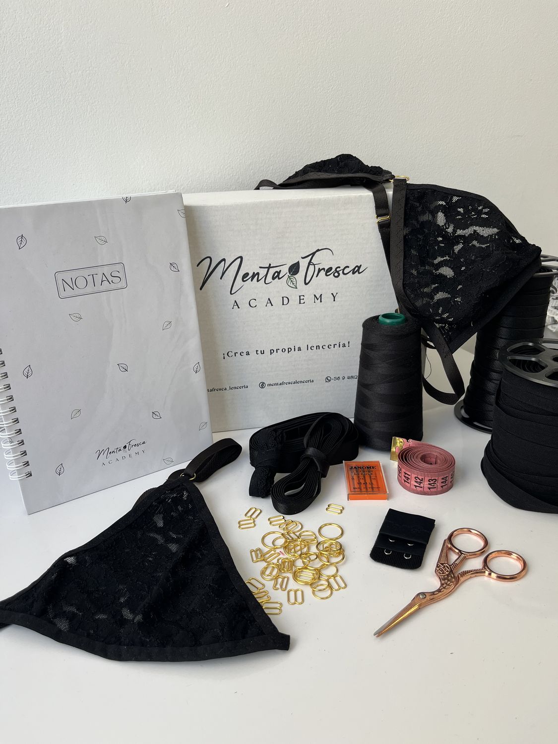 El kit del taller: caja Menta Fresca Academy, cuaderno de notas, bralette y calzón de encaje negro, hilo, elásticos, herrajes dorados, agujas, huincha de medir y tijera.